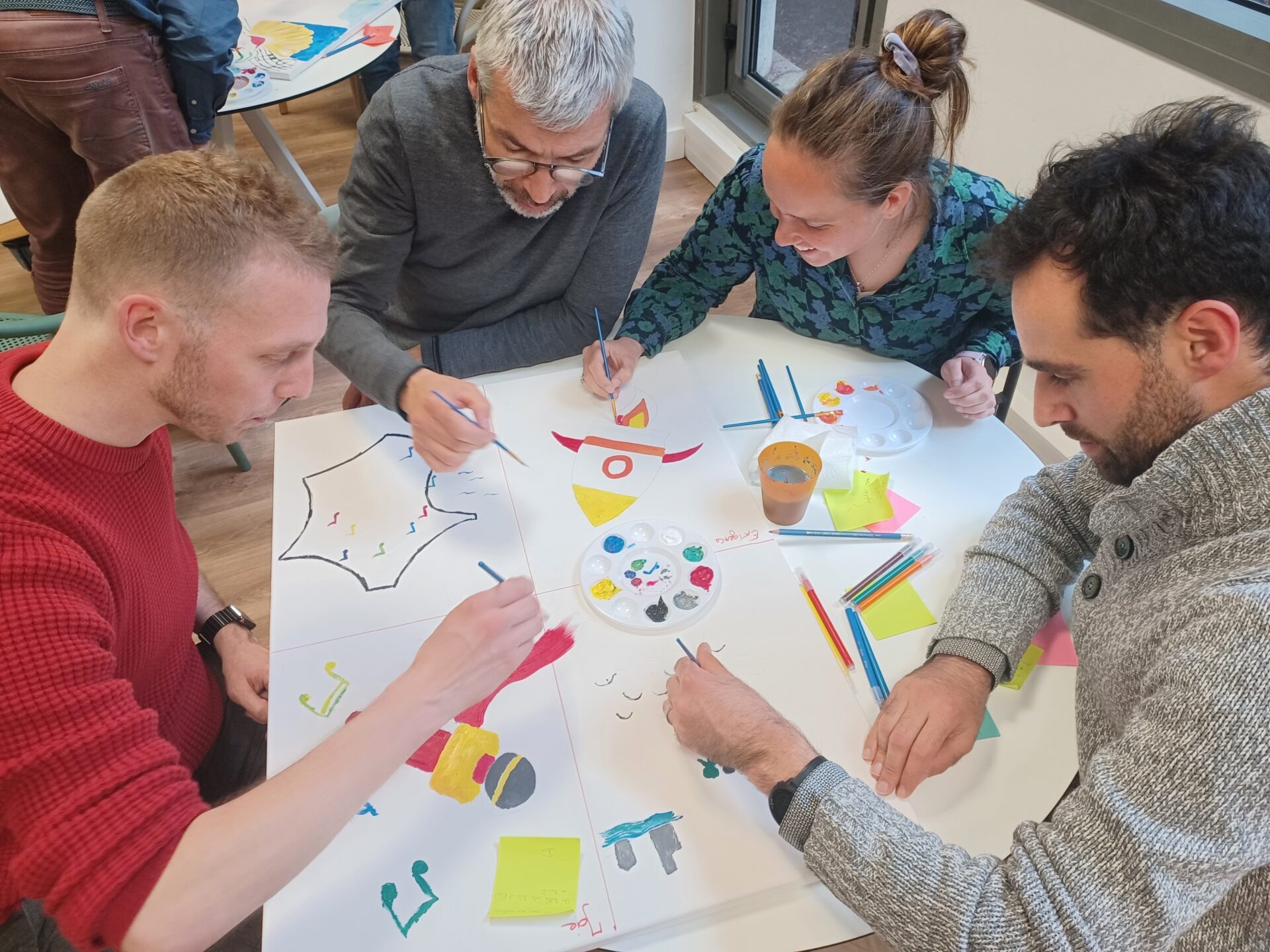 Quatre collègues assis autour d'une table peignant ensemble une fresque collaborative